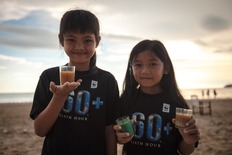 Zwei Kinder halten am Strand drei Gläser Getränke zur Earth Hour 2019