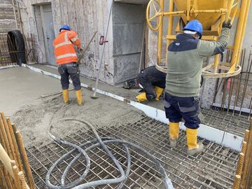 Zwei Bauarbeiter gießen die Betonsohle des neues Betriebsgebäudes.