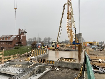 Bild der Baustelle aus der Distanz. Vorne im Bild steht das Bauwerk, dessen Decke nun betonniert wurde. Hinten ist ein Kran zu sehen.