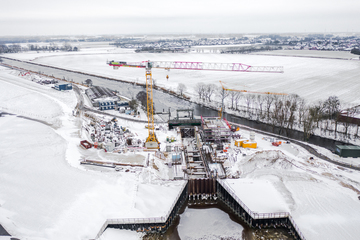 Luftbild der Kanalschleusenbaustelle im Winter. Links ein Baukran. Überall liegt Schnee. Die Schleusenkammer und das Betriebsgebäude sind bereits gut zu erkennen.