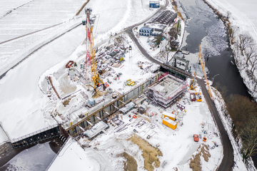 Luftbild der Kanalschleusenbaustelle im Winter. Links ein Baukran. Überall liegt Schnee. Die Schleusenkammer und das Betriebsgebäude sind bereits gut zu erkennen.