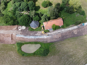 Ein Bagger trägt die alte Winkelstützmauer des Deiches auf Höhe der ehemaligen Mühle in Hönisch ab, bevor dieser Abschnitt verstärkt und erhöht wird. Links schließt der bereits neu profilierte Altdeich an.