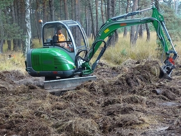 Ein ehemaliger Entwässerungsgraben im Schwarzen Moor wird von Dirk Böckmann mit einem Bagger verschlossen. Teilweise muss Vegetation entfernt werden, um an den darunterliegenden Boden zu kommen. Bereiche mit wertvoller Vegetation werden ausgespart.