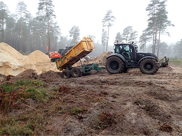 Ein Traktor mit angehängter Mulde kippt den Oberboden in die Vertiefung der späteren sandüberdeckten Verwallung.