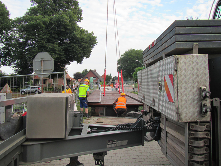 Arbeiter sichern die Brücke, die per Kran engehoben wird.