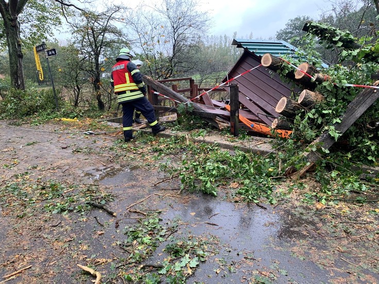 Eine vom Baum getroffene Pegelhütte - daneben stehen zwei Feuerwehrmänner.