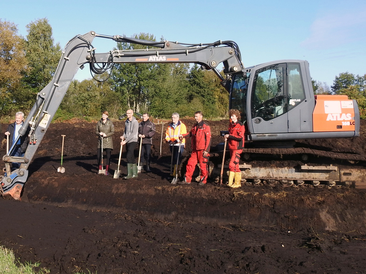 Erster Spatenstich im Moor - Im Hintergrund ein Bagger.