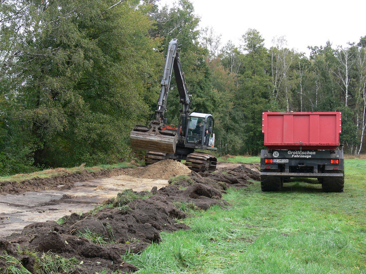 Mit Bagger und Schlepper wird Bodenmaterial für den Bau von Verwallungen gewonnen. Durch die Verwallungen wird Niederschlagswasser im Gebiet zurückgehalten, damit sich artenreiches Nassgrünland entwickeln kann.