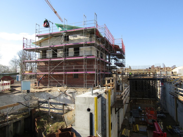 Blick über die Baustelle: links am Dachfirst des noch im Rohbau befindlichen Betriebsgebäudes hängt ein grüner Kranz.