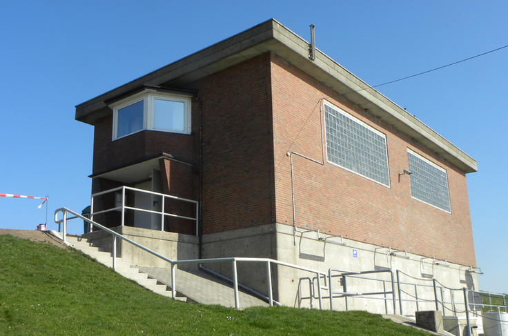 Das Sperrwerksgebäude - ein roter Klinkerbau in einfacher, quadratischer Bauweise. Links der Deich.