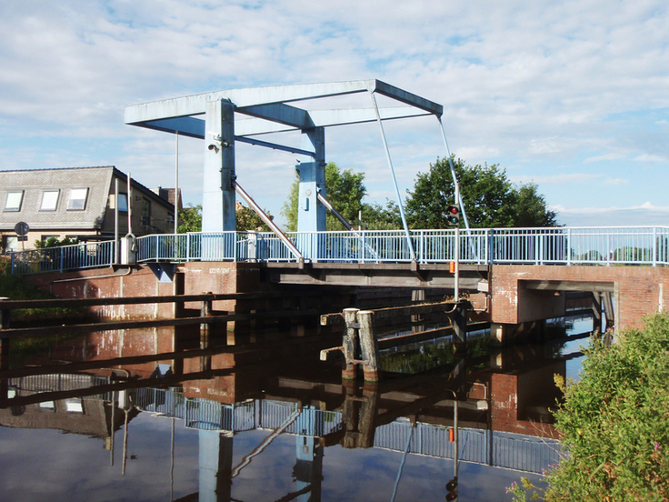 Die Brücke in Wolthusen spiegelt sich im Wasser des Kanals. Im Hintergrund ist Bebauung erkennbar.