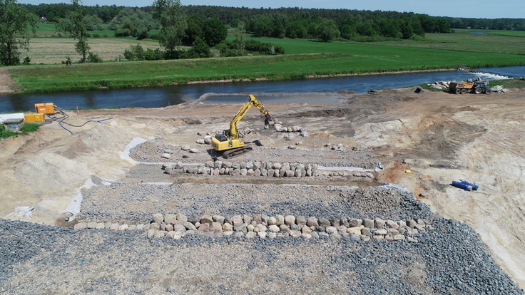 Luftbild: Vorne sind Arbeiten an der neuen Sohle des Raugerinnes erkennbar, während hinten der Fluss in seinem alten, begradigten Bett vorbeifließt.