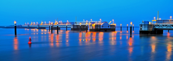 Das Sperrwerk in der Nacht. Die Lichter der Beleuchtung spiegeln sich im Wasser der Ems.