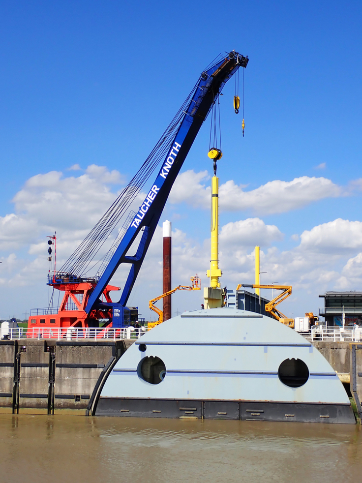 Millimeterarbeit in der Mitte des Flusses: Die per Schwertransport angelieferten Hydraulikzylinder mussten per Schwimmkran an den Nebenöffnungen des Sperrwerks eingebaut werden (Bilder: NLWKN).