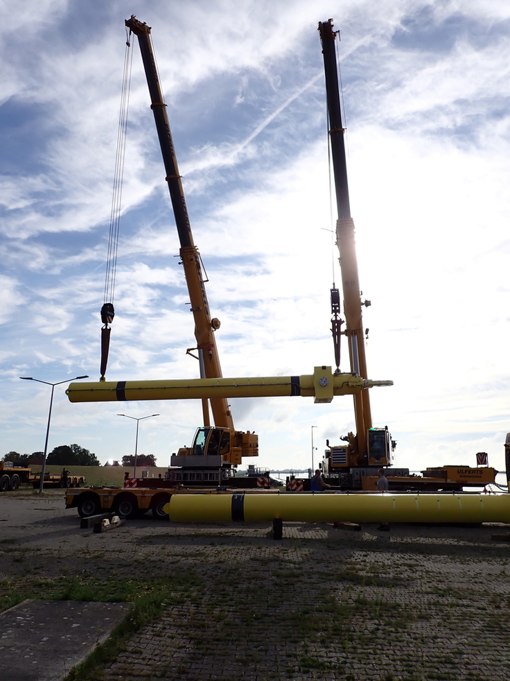 Millimeterarbeit in der Mitte des Flusses: Die per Schwertransport angelieferten Hydraulikzylinder mussten per Schwimmkran an den Nebenöffnungen des Sperrwerks eingebaut werden (Bilder: NLWKN).