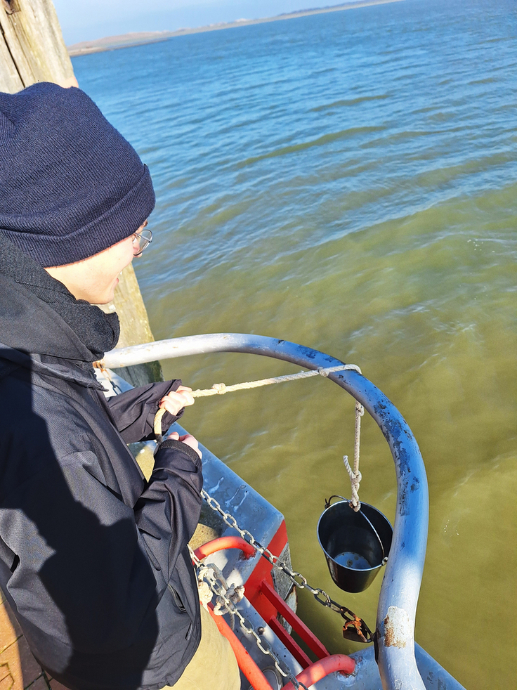 Mit einem Eimer nehmen Phil Beyersdorff und Mia Andermann die Wasserprobe am Norderneyer Hafen. Einige Parameter wie Sauerstoffgehalt und Salinität werden von ihm und Mia Andermann direkt vor Ort bestimmt (Bild: NLWKN).