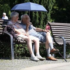 älteres Ehepaar sitzend auf einer Parkbank mit Regenschirm als Sonnenschutz